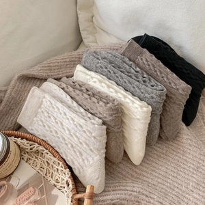 Winter cable knit crew socks in neutral tones neatly stacked on a soft blanket texture