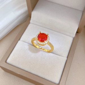 Macro shot of gold-plated halo ring with red round gemstone and pavé zircon accents