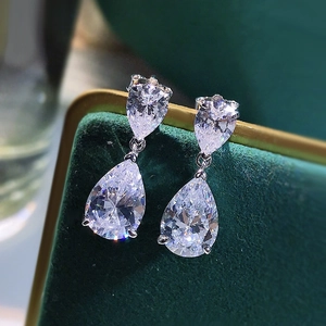 Macro shot of silver teardrop earrings with pear-cut cubic zirconia on green velvet