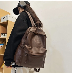 Side view of large brown leather backpack worn by model in a cozy studio setting