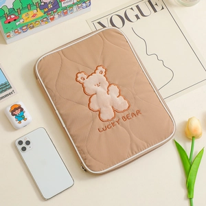 Detail of khaki quilted laptop sleeve featuring embroidered Lucky Bear and lifestyle props