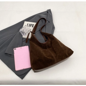 Detail of dark brown hobo bag with suede texture and leather strap next to lifestyle props