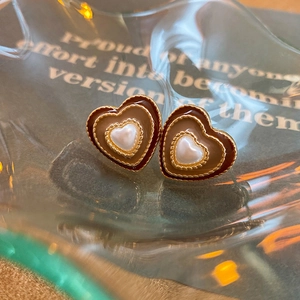 Macro detail of heart earrings with gold metal frame, brown enamel, and central pearl