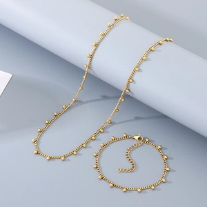 Détail de parure de bijoux en maille gourmette dorée réglable avec billes sur fond neutre