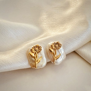 Detail of baroque pearl earrings with gold floral relief on a white silk background