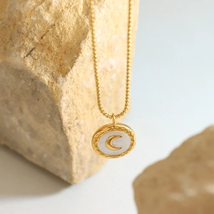 French style gold moon necklace with white shell pendant displayed on natural rocks
