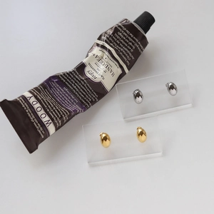 Polished gold and silver teardrop stud earrings displayed on acrylic jewelry stands