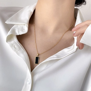 Detail of a minimalist gold necklace with a black rectangular pendant worn on a model
