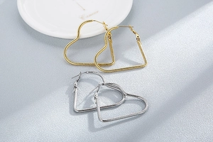 Detailed view of large heart-shaped gold and silver earrings with textured twist surface