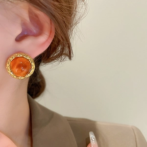 Detail of vintage round amber resin earring with gold textured border on female model
