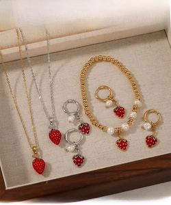 Detailansicht des Erdbeer-Schmucksets mit roten Emaille-Anhängern an Halskette und Ohrringen