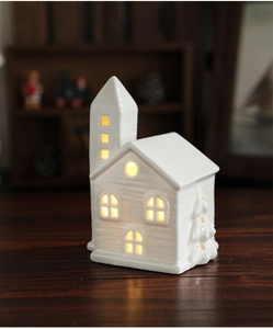 Detail of warm glowing ceramic Christmas house ornament on blurred wood background