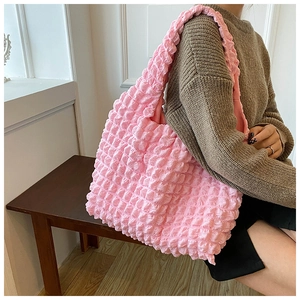 Pink bubble texture shoulder bag carried by model wearing a brown knit sweater