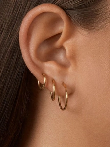 Gros plan de trois tailles de créoles en acier inoxydable plaqué or 18 carats sur l'oreille