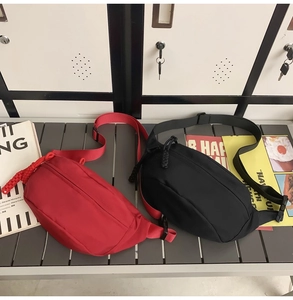 Detail of red and black minimalist nylon crossbody bags on a grey bench with urban props