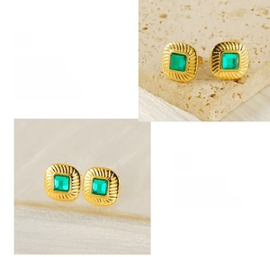 Detail of square gold-plated earrings with emerald zircon and polished metal texture