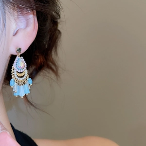 Close-up of bohemian fan-shaped drop earrings with colorful crystals and blue tassels