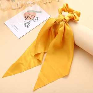 Close-up of bright yellow satin scrunchie with long ribbons on a cream display stand