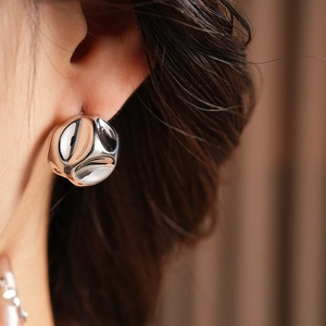 Close-up of a silver sculptural pleated stud earring worn for a minimalist stylish look