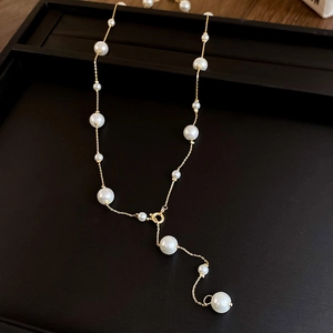 Detailed view of elegant gold Y-shaped faux pearl necklace on black jewelry tray