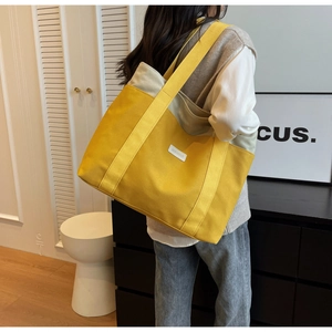 Detailed view of large yellow canvas tote bag with dual straps on a model in a modern home