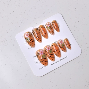 Detail of semi-handmade almond fake nails with tiger stripes and 3D floral accents