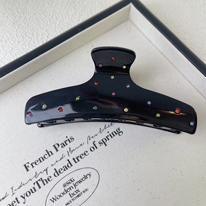 Detailed shot of black acetate shark clip featuring colorful rhinestones on a beige paper