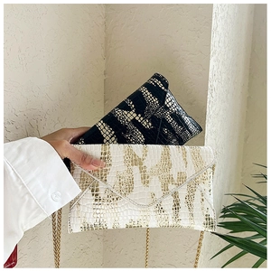 Detail of crocodile pattern envelope clutch bags in black and white with gold chain strap
