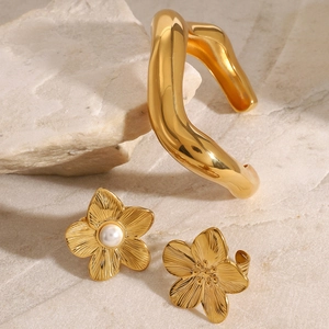 Golden irregular wavy open bangle set with pearl flower earrings on white rock base