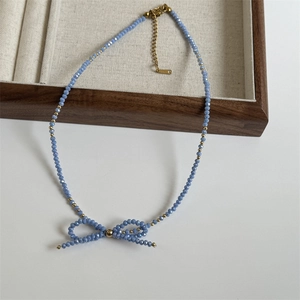 Macro shot of light blue faceted beads necklace featuring a delicate bow pendant and gold accents