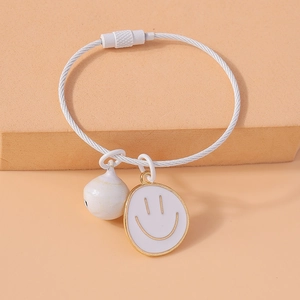 Detail view of white wire bracelet featuring a smiley face and ball pendant on beige surface