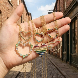 Golden heart pendant necklaces with colorful zircon stones held against a sunlit background