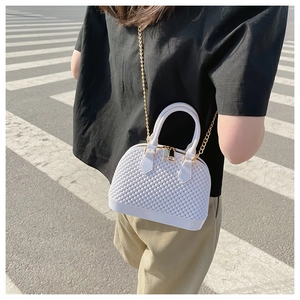 Detail of white PVC shell bag with pearl texture and golden chain on a street background