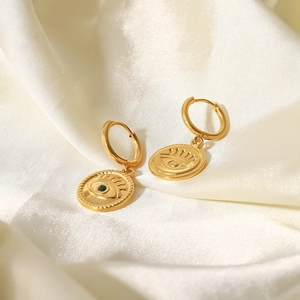 Detail of 18K gold-plated evil eye earrings with green stone on white silk fabric