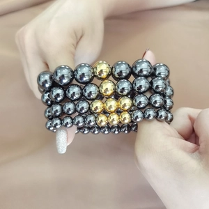 Close-up of a multi-layer magnetic bracelet with dark grey beads and gold accents