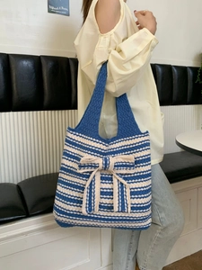 Close-up of blue and white striped knit tote bag featuring a large decorative 3D bow