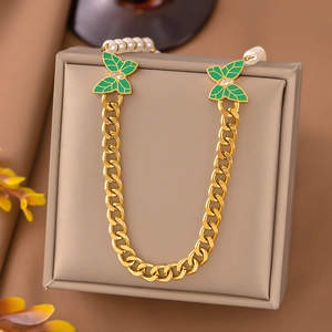 Macro detail of golden cuban chain necklace featuring green enamel butterflies and pearls