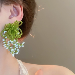 Detail shot of green and white handmade beaded floral earrings worn by a model