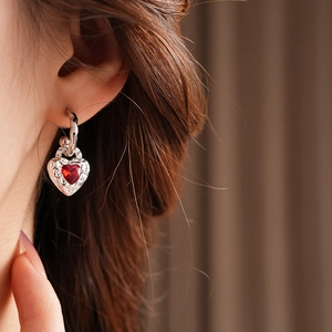 Close-up of model wearing silver heart earrings with a red gemstone and vintage texture