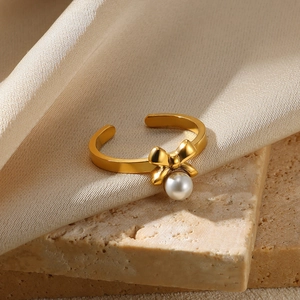 Detailed shot of golden bowknot ring with white pearl on beige stone and silk background
