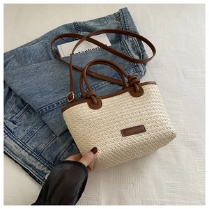 Fashionable woven crossbody tote bag in beige with dark brown handles on denim background