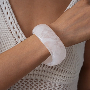 Detailed view of chunky acrylic bangle with white marble texture on a model wrist