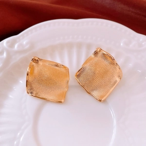 Macro detail of gold-plated square earrings with mesh texture on elegant ceramic plate