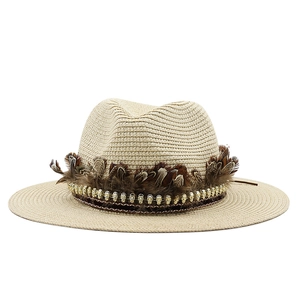 Detail of wide brim straw hat with brown feathers and golden skull charms decor