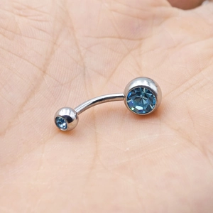 Polished stainless steel curved belly ring with dual blue faceted crystals held in palm