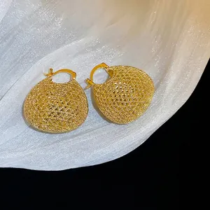 Elegant gold woven hollow ball earrings on white silk fabric with luxury metal texture