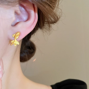 Gros plan d'une boucle d'oreille dorée en forme de poisson portée par un mannequin