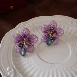 Gros plan détaillé des boucles d'oreilles fleurs mauves avec cristal bleu sur porcelaine