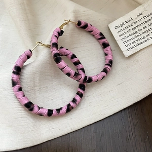 Gros plan de grandes créoles tressées à motif zèbre rose et noir sur un tissu texturé