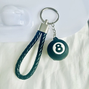 Miniature black number 8 pool ball keychain with woven leather strap on white fabric